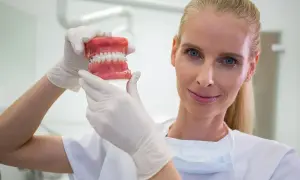 Dentystka w białej rękawiczce pokazuje model szczęki z aparatem ortodontycznym, zastanawiając się, ile zarabia dentysta.