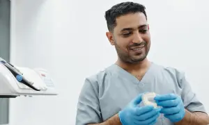 Uśmiechnięty technik dentystyczny w niebieskich rękawiczkach trzyma przezroczystą nakładkę na zęby.