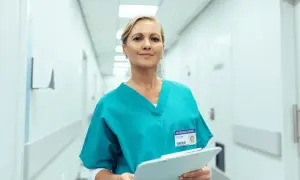 Uśmiechnięta farmaceutka w turkusowym uniformie trzyma dokumenty. Zastanawiasz się, ile zarabia farmaceuta?