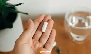 Dłoń trzyma białą kapsułkę. Obok szklanka wody i roślina. Uważaj na nadmiar magnezu objawy.
