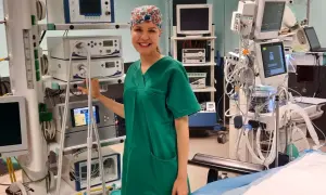 Uśmiechnięta instrumentariuszka w zielonym uniformie stoi obok aparatury medycznej na sali operacyjnej.
