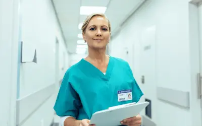 Uśmiechnięta farmaceutka w turkusowym uniformie trzyma dokumenty. Zastanawiasz się, ile zarabia farmaceuta?