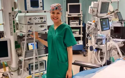 Uśmiechnięta instrumentariuszka w zielonym uniformie stoi obok aparatury medycznej na sali operacyjnej.