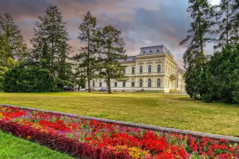 Piękny budynek sanatorium otoczony drzewami i kolorowymi kwiatami. Dowiedz się o nowe zasady wyjazdu do sanatorium na NFZ.