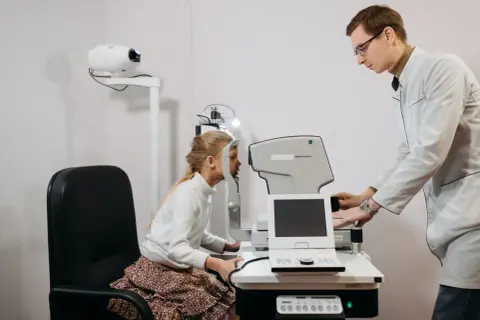 Okulista bada wzrok dziewczynki. Czy do okulisty potrzebne jest skierowanie? Zwykle nie, ale warto sprawdzić.