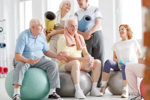 Grupa seniorów po zajęciach rehabilitacja kardiologiczna, odpoczywa na piłkach gimnastycznych, trzymając butelki z wodą.