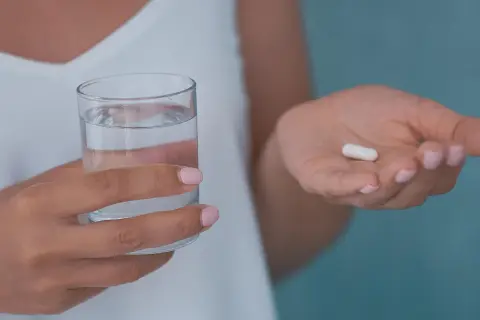 Dłoń trzymająca szklankę wody i białą kapsułkę, która może być jednym z neuroleptyków.