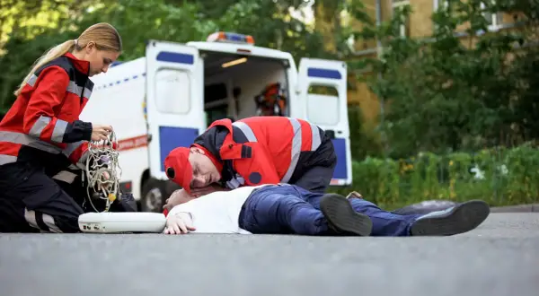 Ratownicy medyczni udzielają pomocy osobie nieprzytomnej na drodze, obok otwartej karetki.