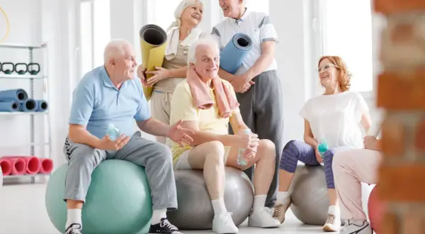 Grupa seniorów po zajęciach rehabilitacja kardiologiczna, odpoczywa na piłkach gimnastycznych, trzymając butelki z wodą.