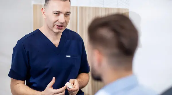 Dentysta w granatowym uniformie pokazuje pacjentowi model szczęki.