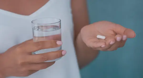 Dłoń trzymająca szklankę wody i białą kapsułkę, która może być jednym z neuroleptyków.