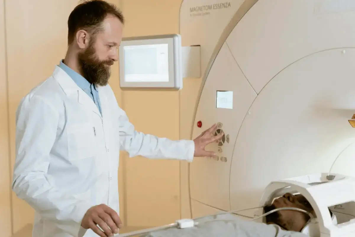 Technik elektroradiolog zarobki: mężczyzna w białym fartuchu obsługuje aparat MRI, na którym leży pacjent.