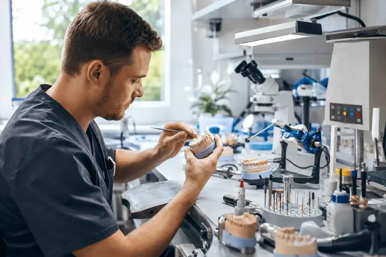 Technik dentystyczny pracujący nad modelem zębów. Jego precyzja przekłada się na dobre technik dentystyczny zarobki.