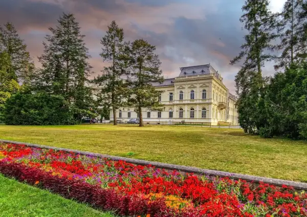 Piękny budynek sanatorium otoczony drzewami i kolorowymi kwiatami. Dowiedz się o nowe zasady wyjazdu do sanatorium na NFZ.