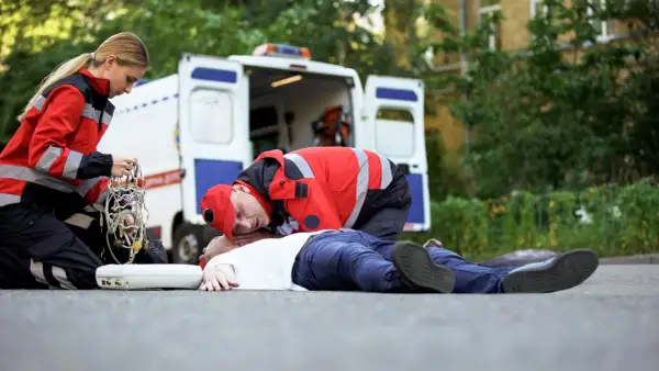Ratownicy medyczni udzielają pomocy osobie nieprzytomnej na drodze, obok otwartej karetki.