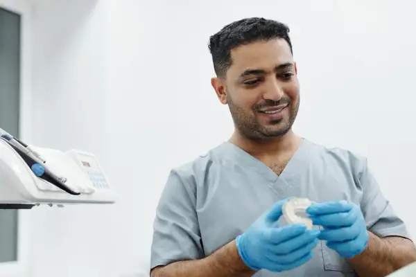 Uśmiechnięty technik dentystyczny w niebieskich rękawiczkach trzyma przezroczystą nakładkę na zęby.