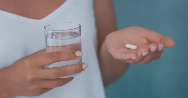 Dłoń trzymająca szklankę wody i białą kapsułkę, która może być jednym z neuroleptyków.